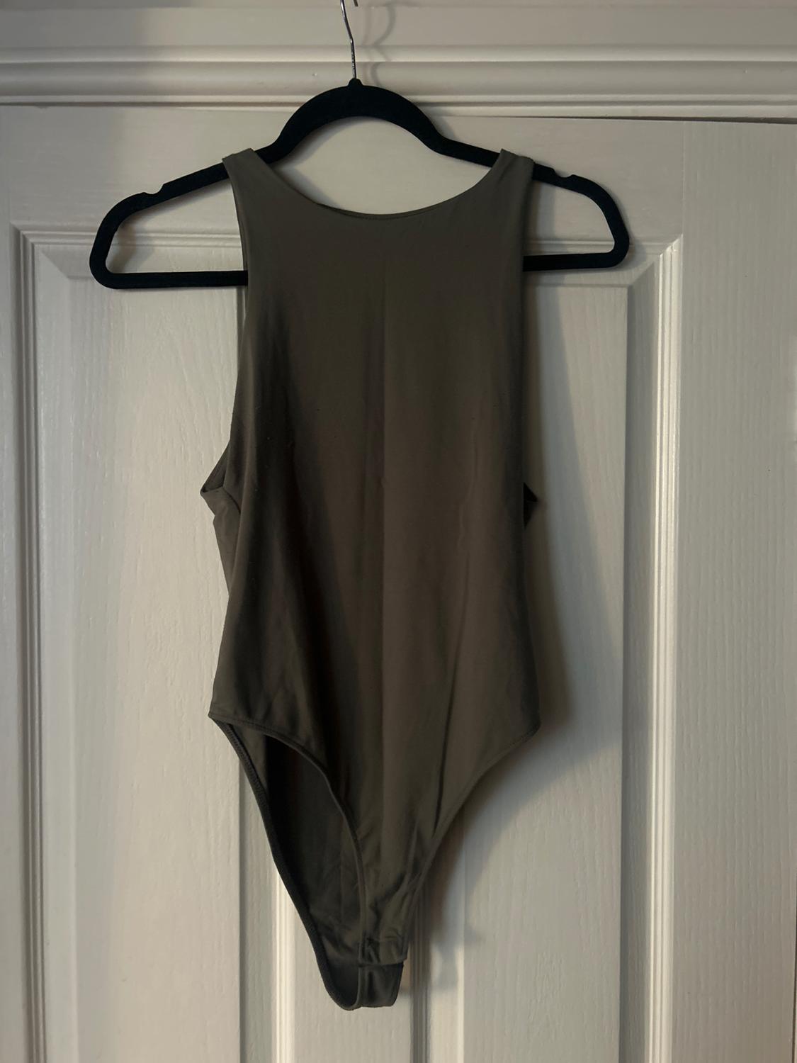Dark grey bodysuit hanging on a black hanger over a white door. Light creates soft shadows on the fabric.