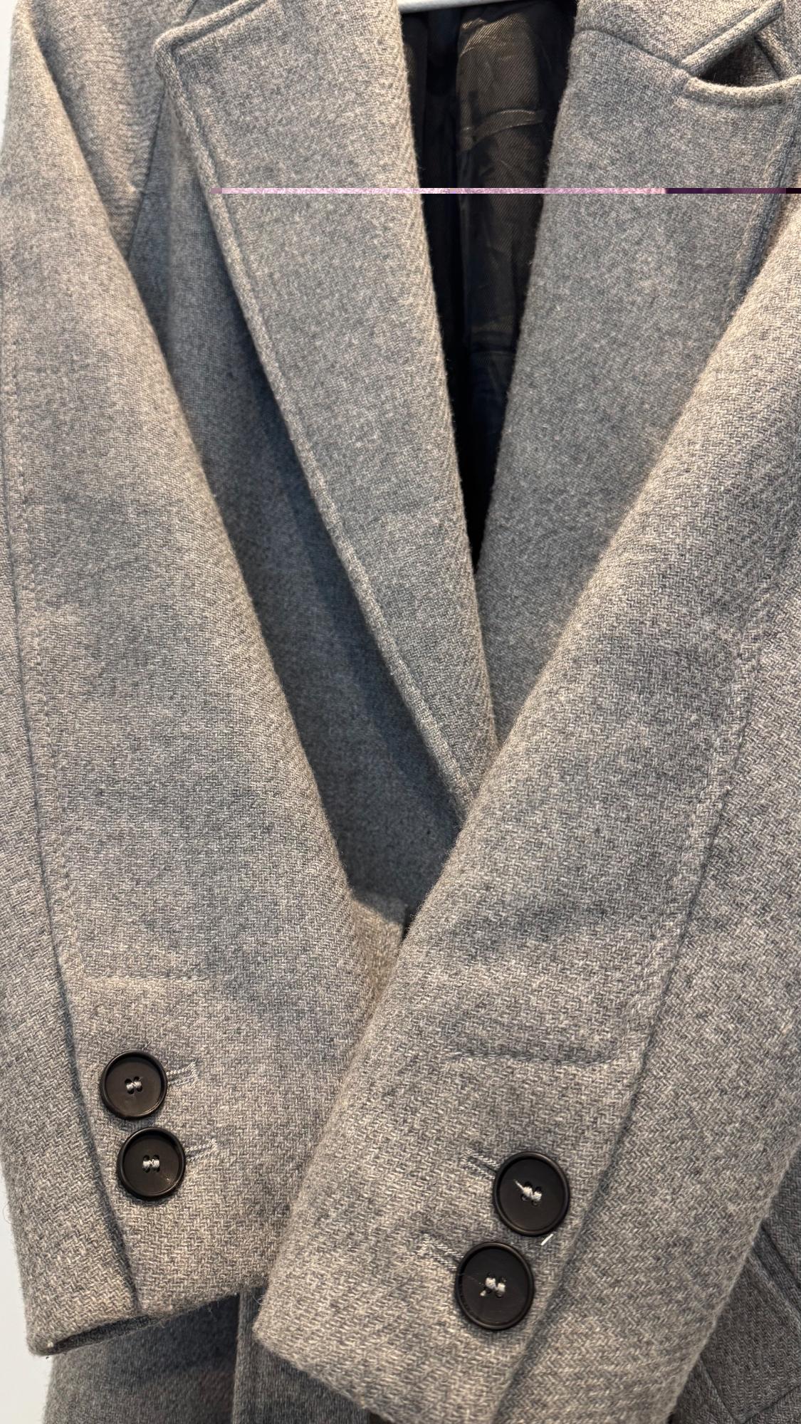 Grey coat with wide lapels and black buttons, hanging on a hanger. Soft-textured fabric and classic design.