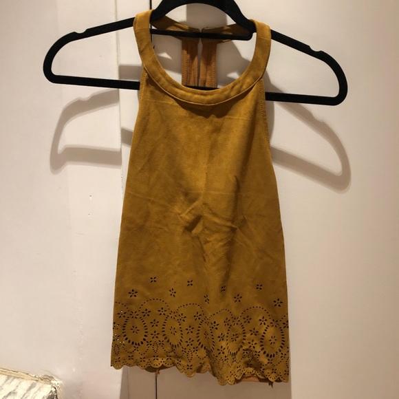 Mustard halter neck top with floral laser-cut hem, hanging on a black hanger against a white door with shadows. Casual style.