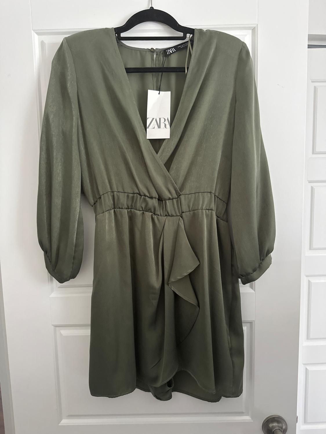 Olive green mini dress with a crossover neckline, long puff sleeves and tie waist detail, hanging on a black hanger.