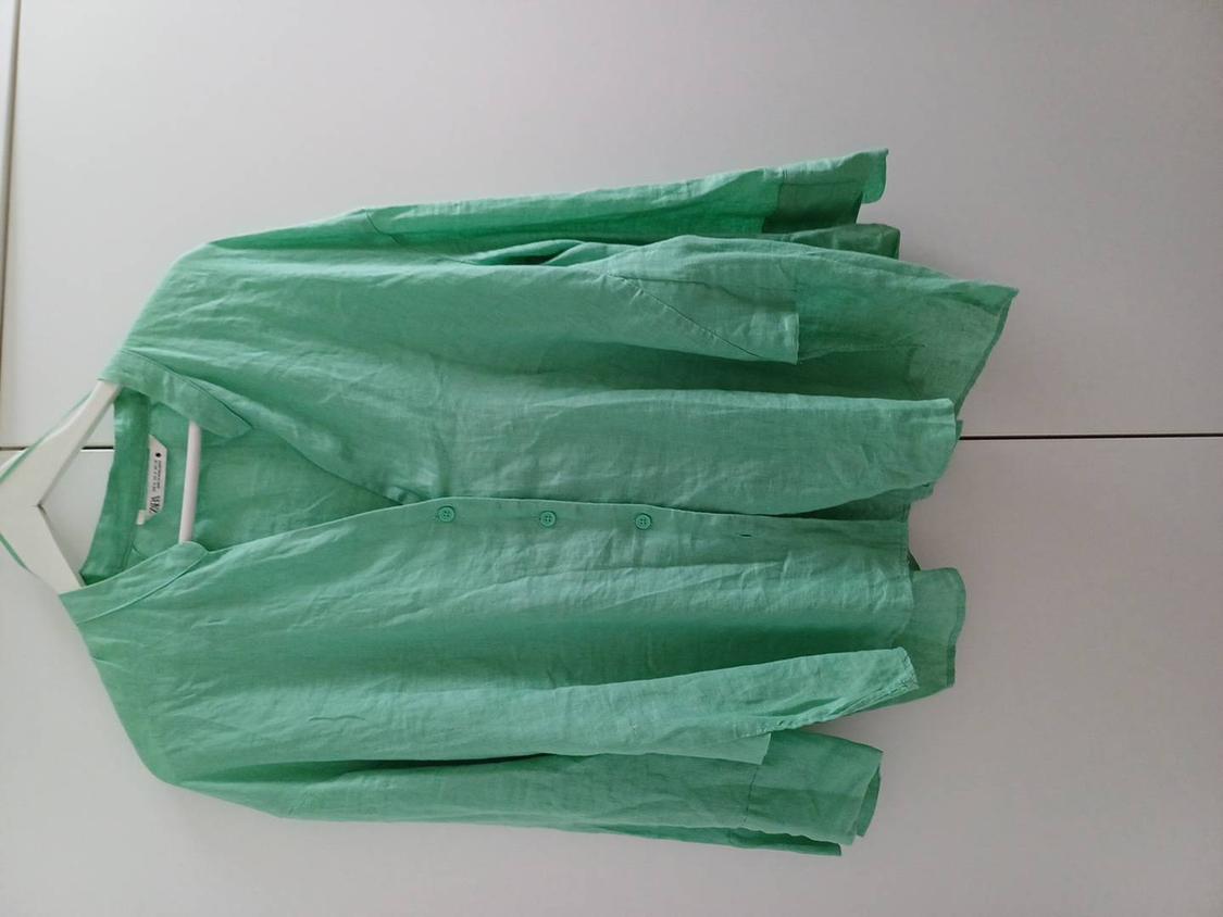 Green linen shirt hanging on a white hanger against a white background. The label shows partially visible text.
