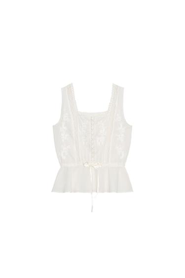 Front view of a sleeveless white blouse with floral embroidery and a waist tie.