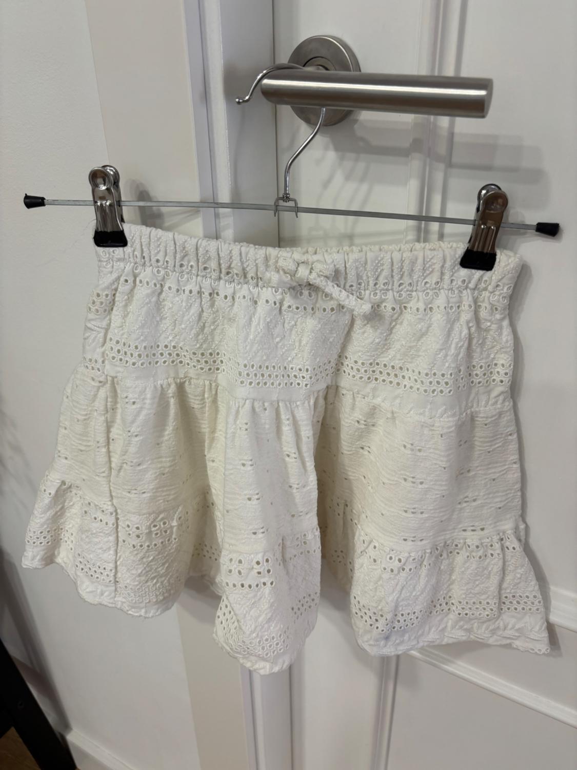 White lace mini skirt hanging on a hanger over a white door with a silver handle.