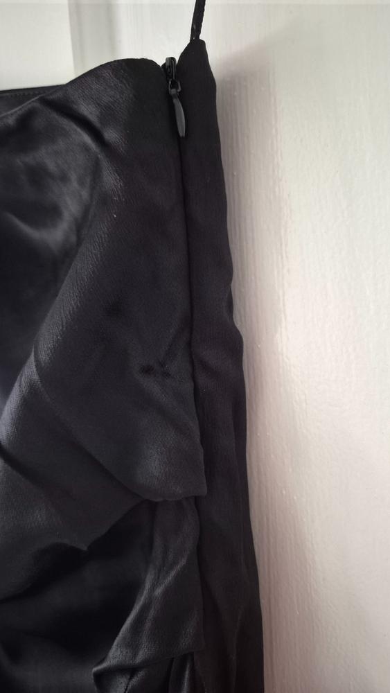 Detail of a black garment with a satin texture and zip fastening, hanging on a white wall.