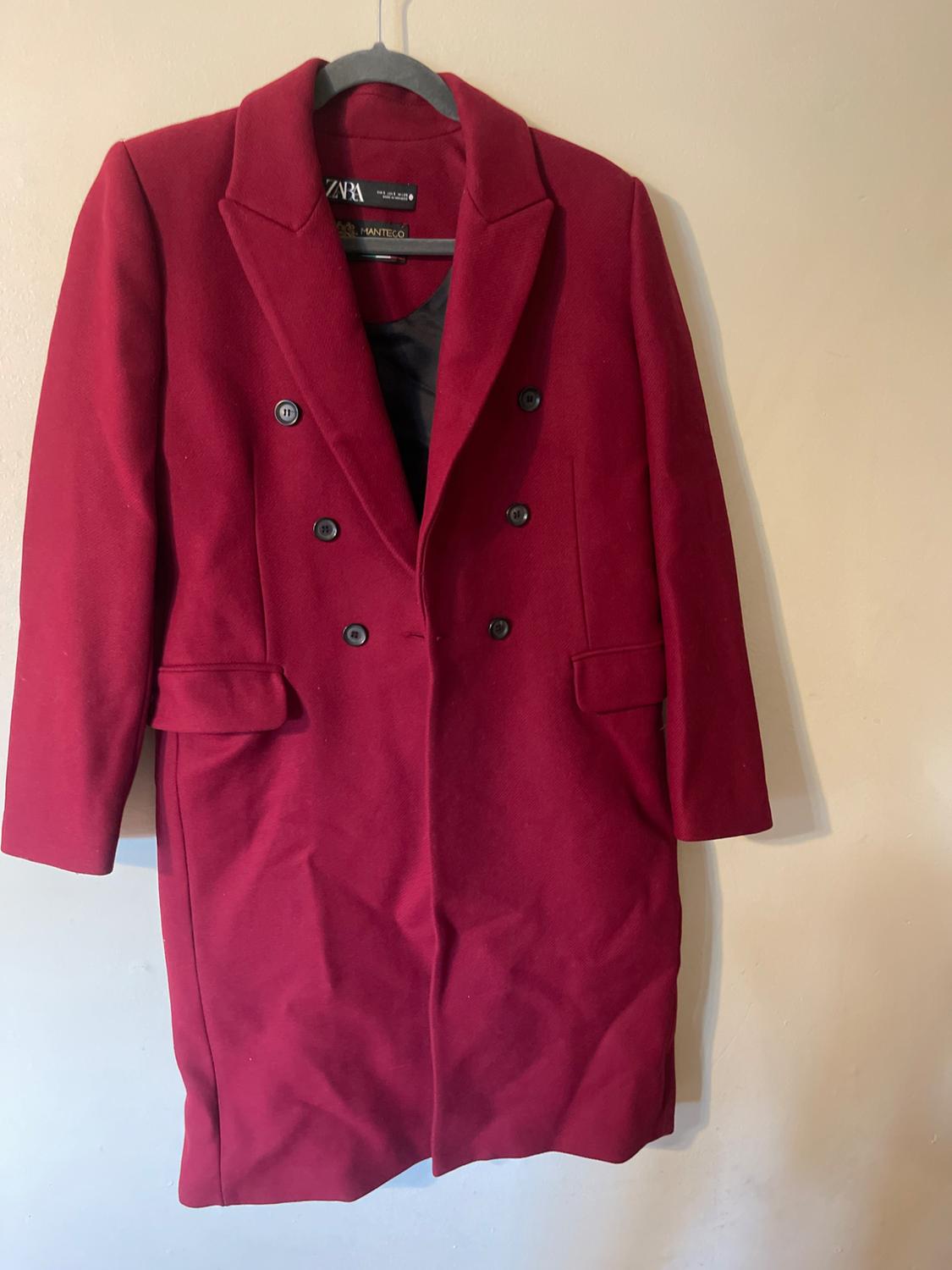 Red double-breasted coat hanging on a black hanger. Visible label on the inside of the collar. White background.