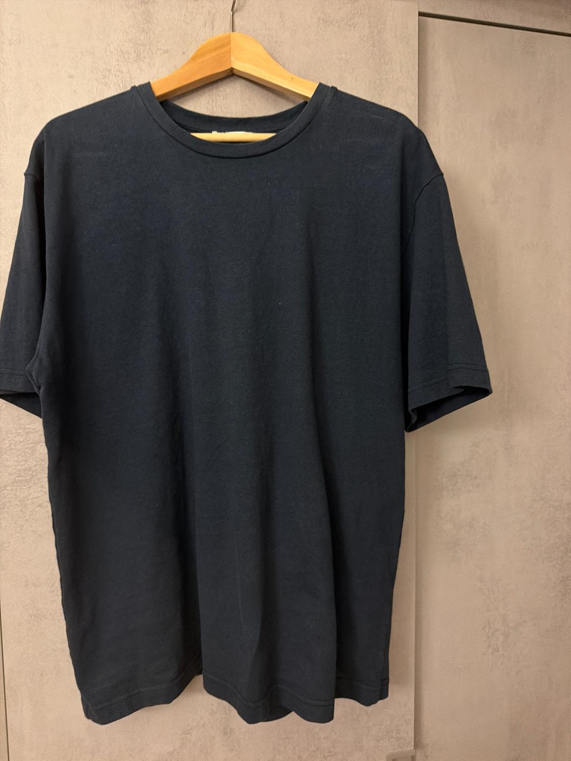 Basic short-sleeved T-shirt in dark blue, hanging on a wooden hanger against a light, textured wall.
