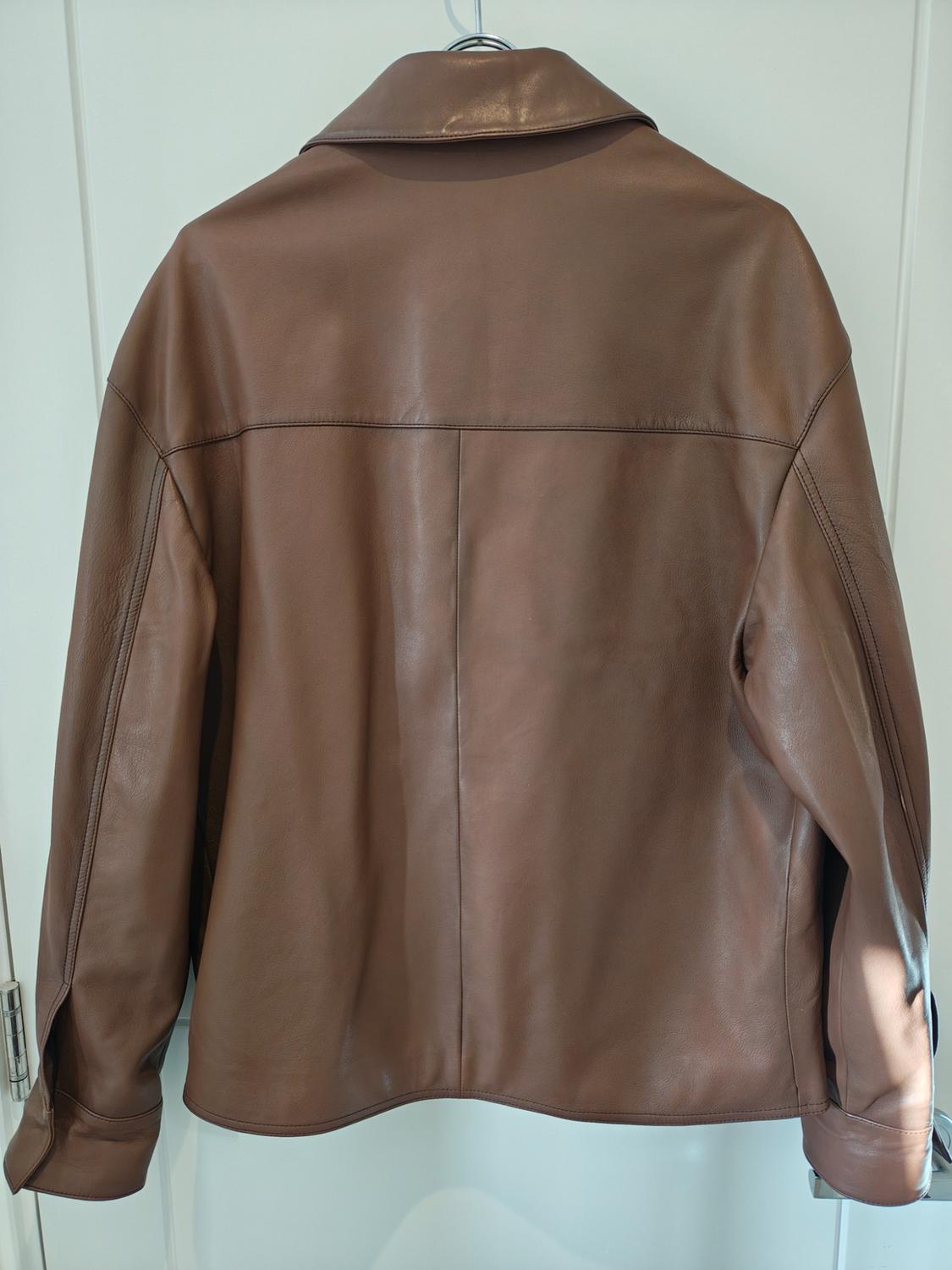 Brown leather jacket hanging on a hanger, rear view, with white background.