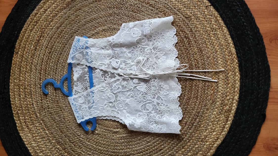 White lace top with ties, hanging on a blue hanger above a round jute rug in brown and black tones.