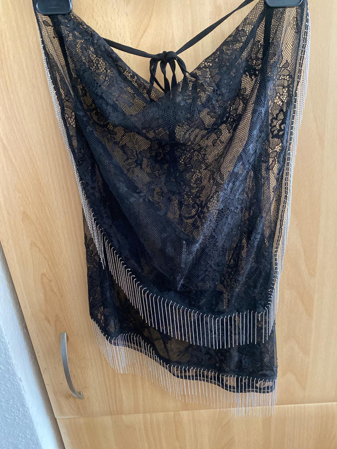Sparkly fringed black lace dress hanging on a hanger over a light wooden door.
