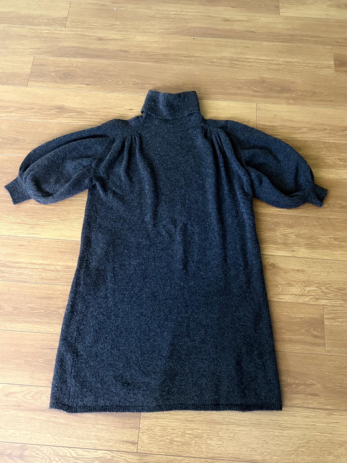 Dark grey knitted dress with a high neck and puffed sleeves, spread out on a light wooden floor.