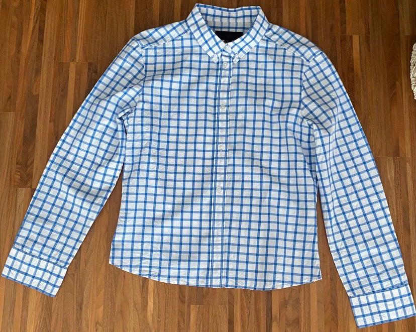 Long-sleeved shirt in blue and white checks, buttoned up, laid out on a wooden floor.