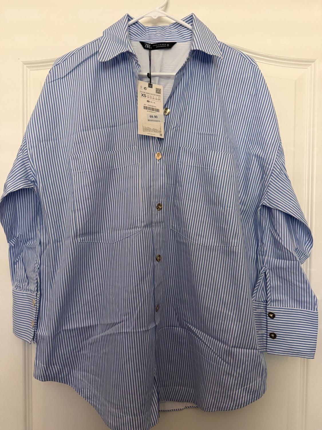 Blue and white striped shirt hanging on a white door. Sleeves with openings. Text: ZARA EUR XS USA XS MEX 24 XS 69.90