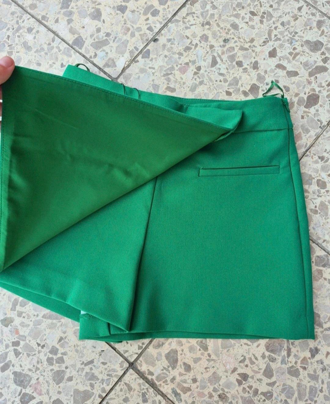 Hand lifting the flap of a bright green skort on a terrazzo floor, revealing the shorts underneath.