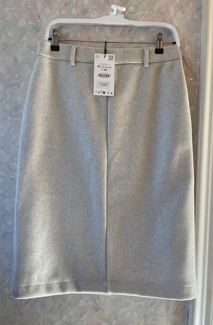 Light grey skirt hanging on a white hanger with a visible tag. Faint floral-patterned wall in the background.