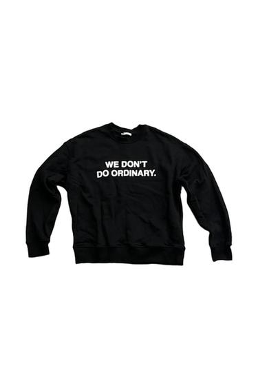 Black crewneck sweatshirt on a white background with the text "WE DON'T DO ORDINARY." printed in the center.