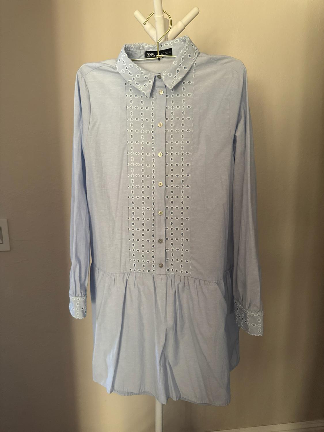 Light blue shirt dress on a hanger. It has long sleeves and
eyelet embroidery on the front panel, collar, and cuffs. ZARA label visible.