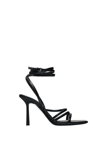 Side view of a black sandal with a high heel and thin ankle straps.