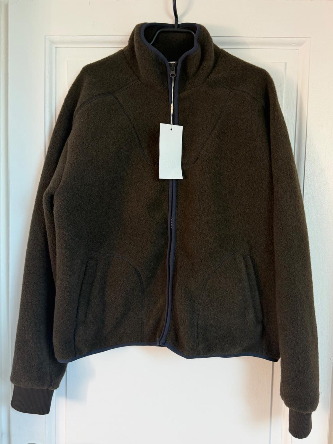 Brown wool jacket with a zip and high collar, hanging on a hanger. White label visible in the centre.