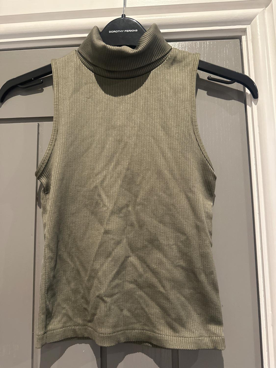Olive green ribbed sleeveless top with a high neck, hanging on a black Dorothy Perkins hanger over a grey door.