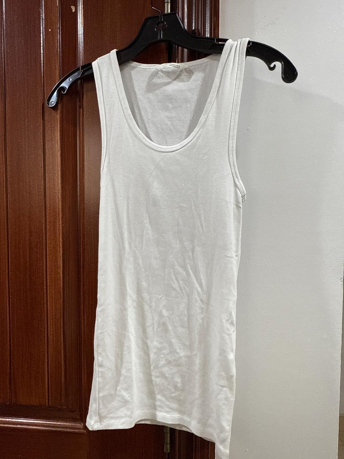 White tank top hanging on a black hanger on a wooden door. White wall background.