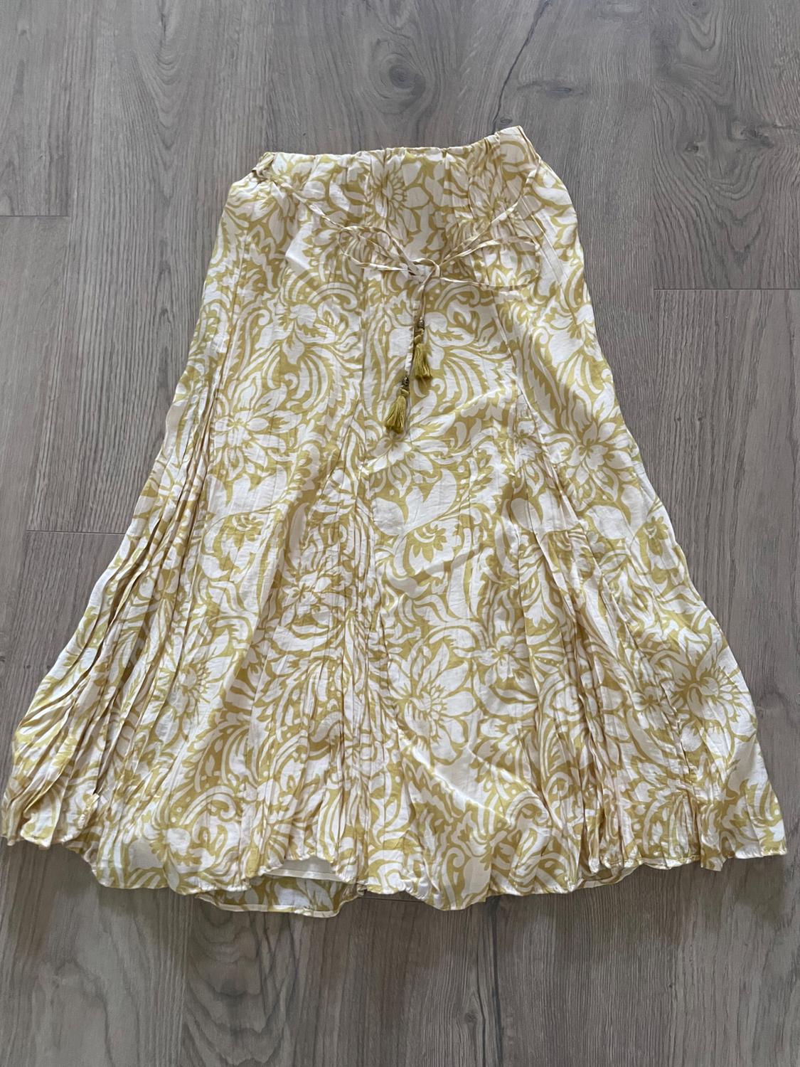 Pleated skirt with yellow floral print on a white background, placed on a gray wooden floor.
