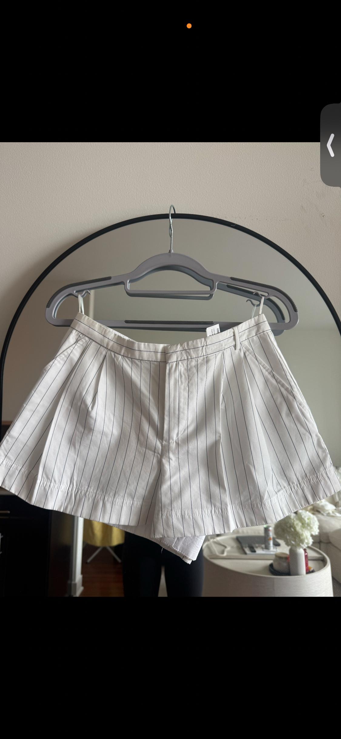 White shorts with black stripes hanging on a grey hanger in front of a round mirror in a modern room.