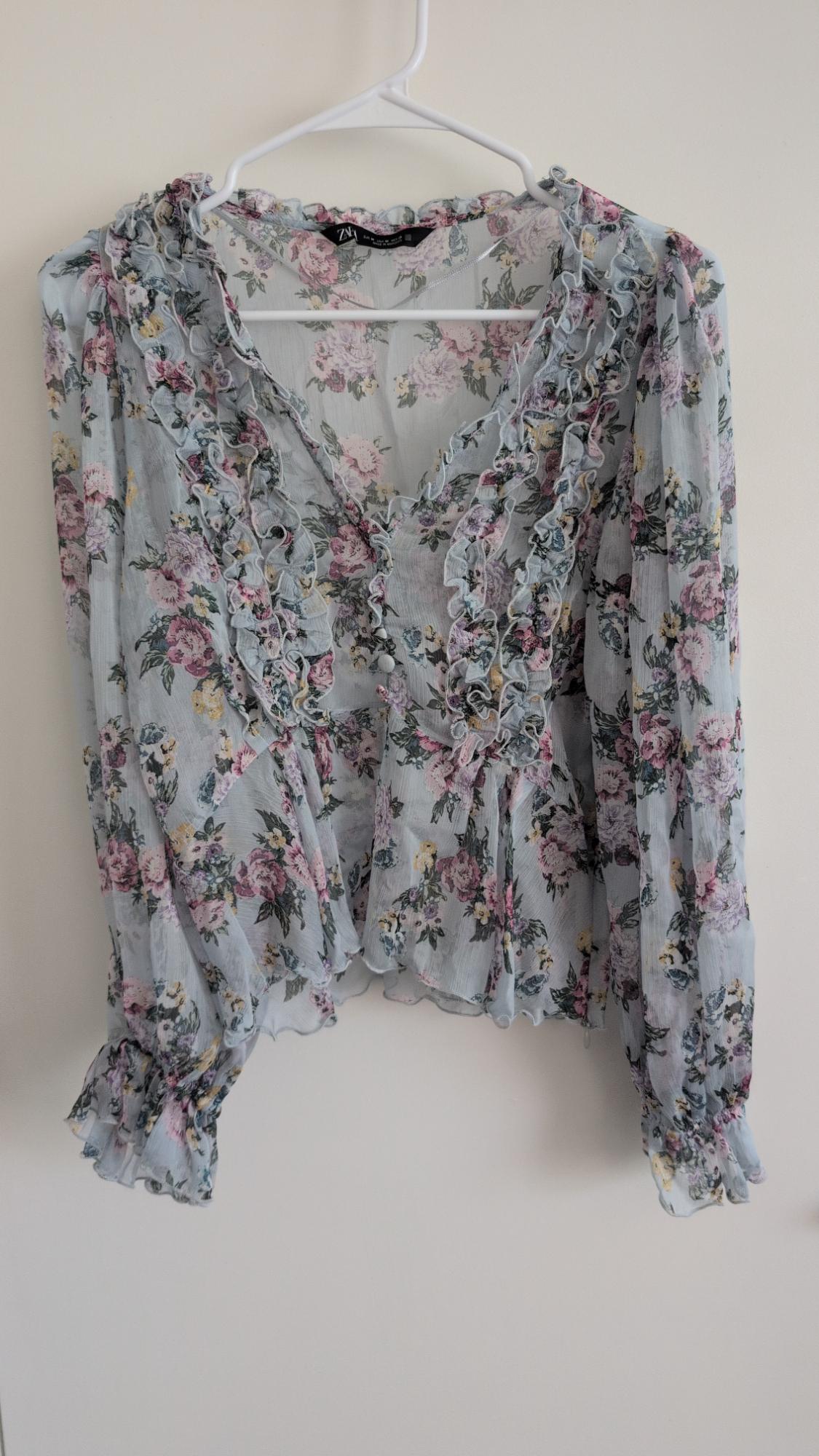 Light blue floral print blouse with a V-neck, ruffles, and long sleeves, hanging on a white hanger.