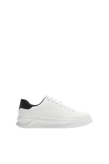 Side view of a white trainer with a black heel and white sole.