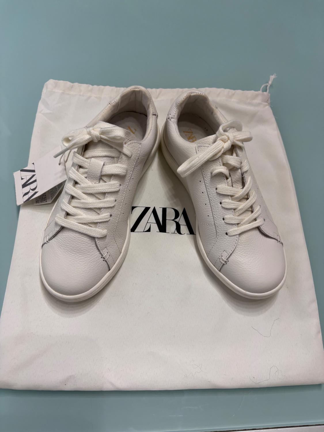 White lace-up trainers on a white canvas bag with the "ZARA" logo. Label visible on the left.