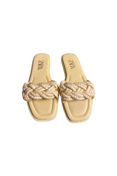 Beige flat sandals with thick braided straps and a square sole. Visible text: "ZARA" on the insole. White background.