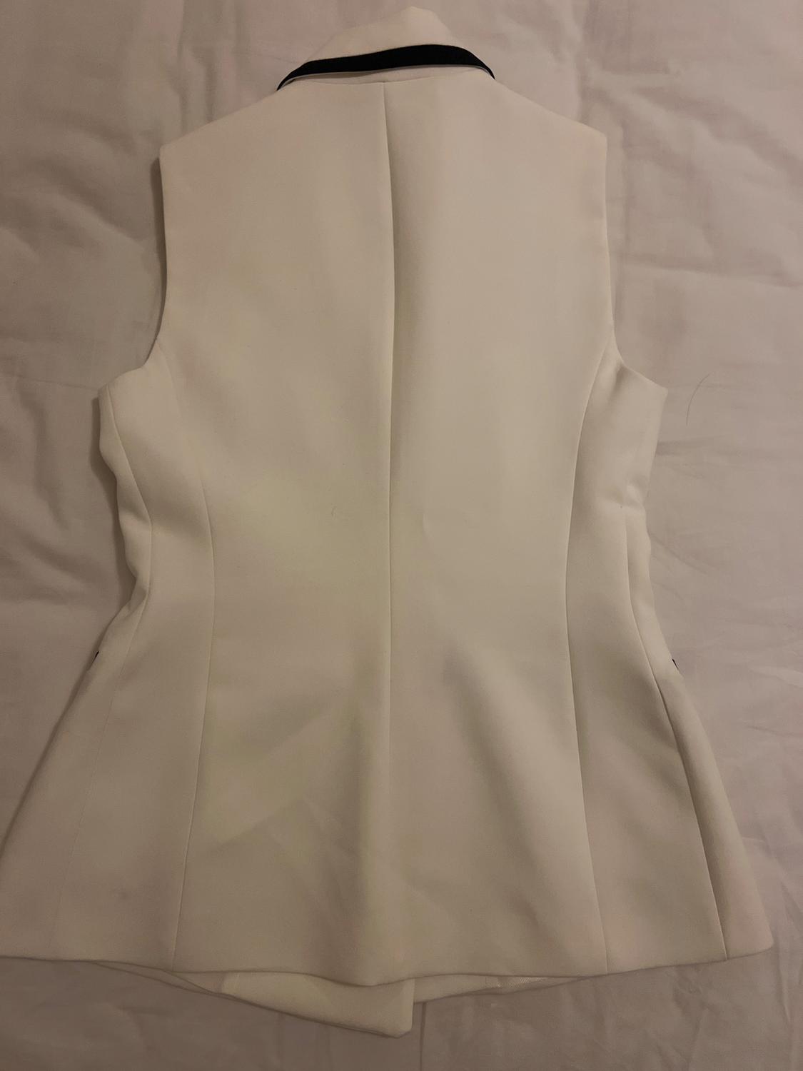 White, sleeveless waistcoat with a black collar, viewed from the back, on a white surface.