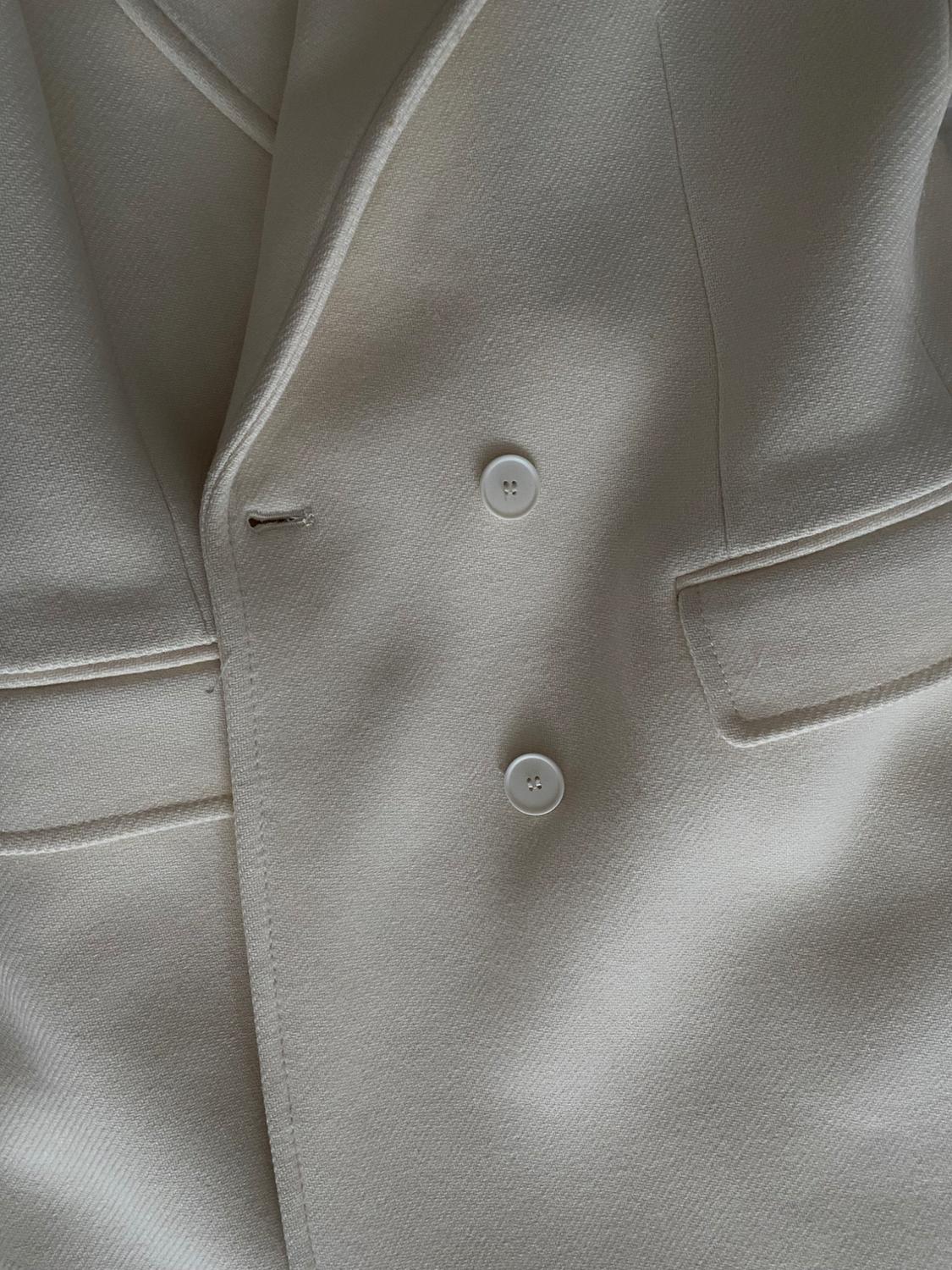 Close-up of a textured cream-coloured jacket. It shows two front buttons, part of the lapel, and side pockets.