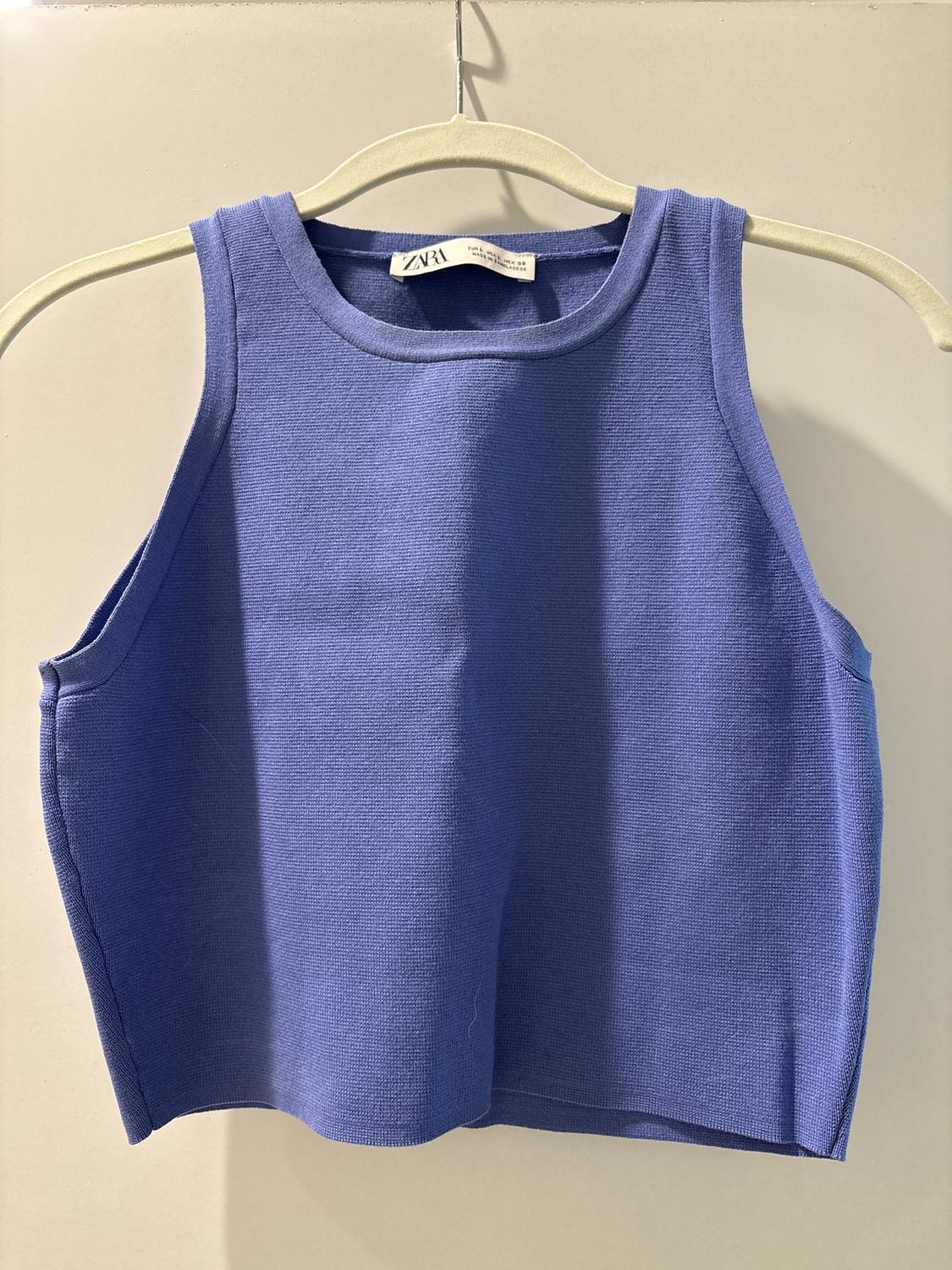 Blue sleeveless top hanging on a beige hanger. Visible tag with text "ZARA". Neutral background.