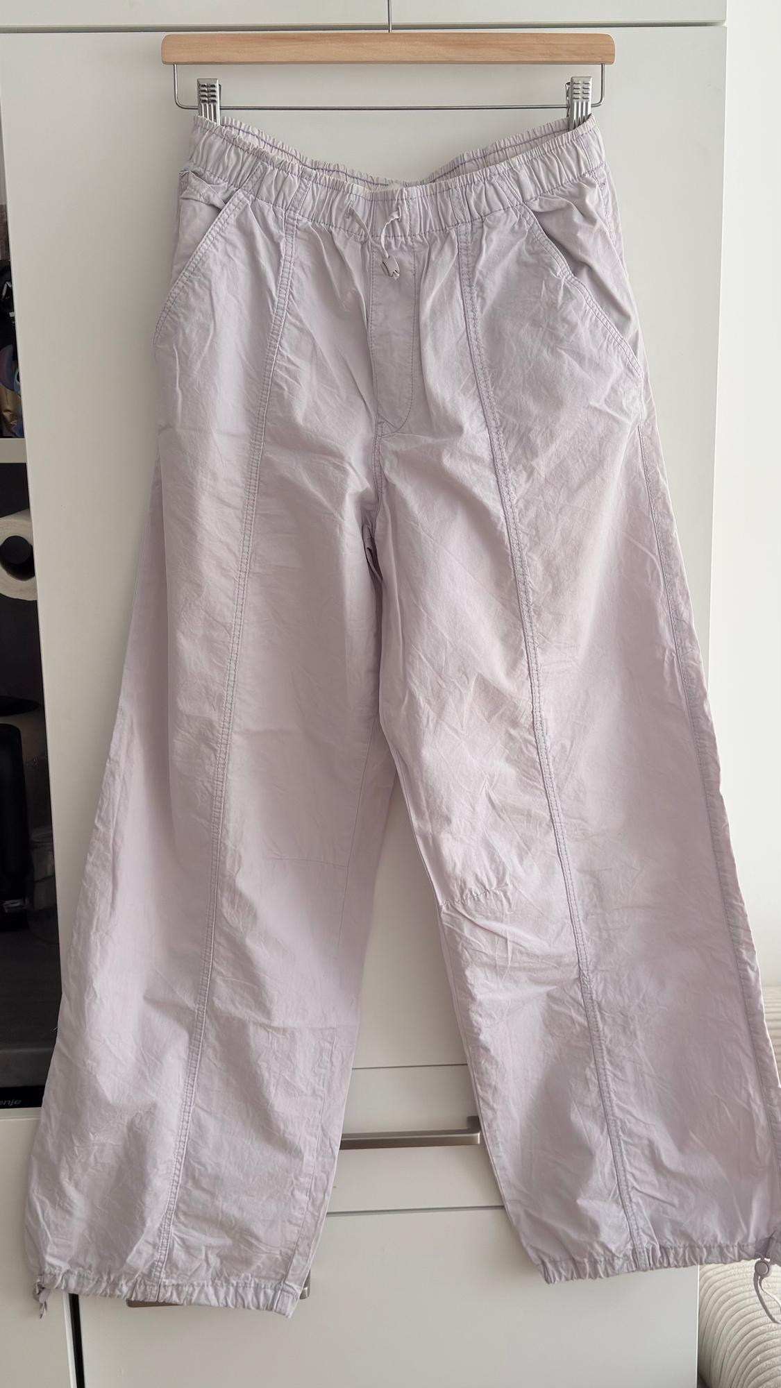 Light-coloured wide-leg trousers hung on a wooden hanger, with an elasticated waist and side pockets. White background.