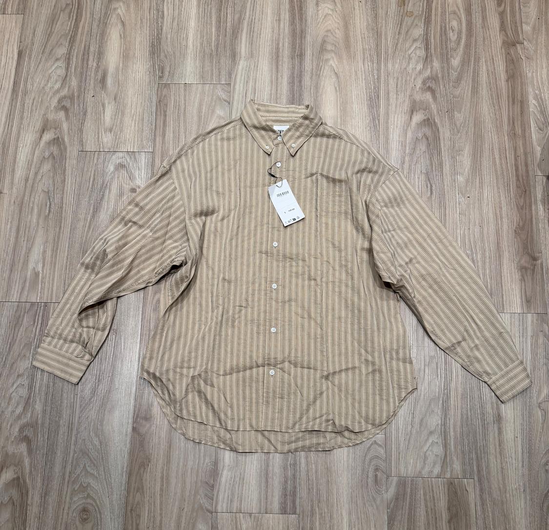 Beige striped shirt with button-down collar and hang tag on light wooden flooring.