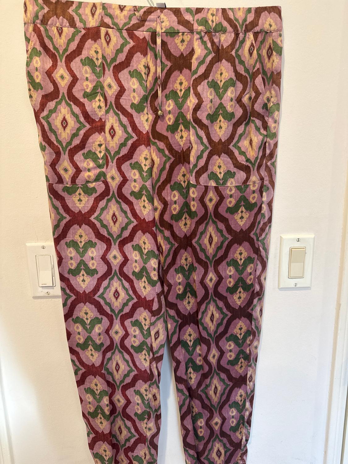 Trousers with a geometric print in purple, green, and yellow tones, hanging on a white wall with visible light switches.