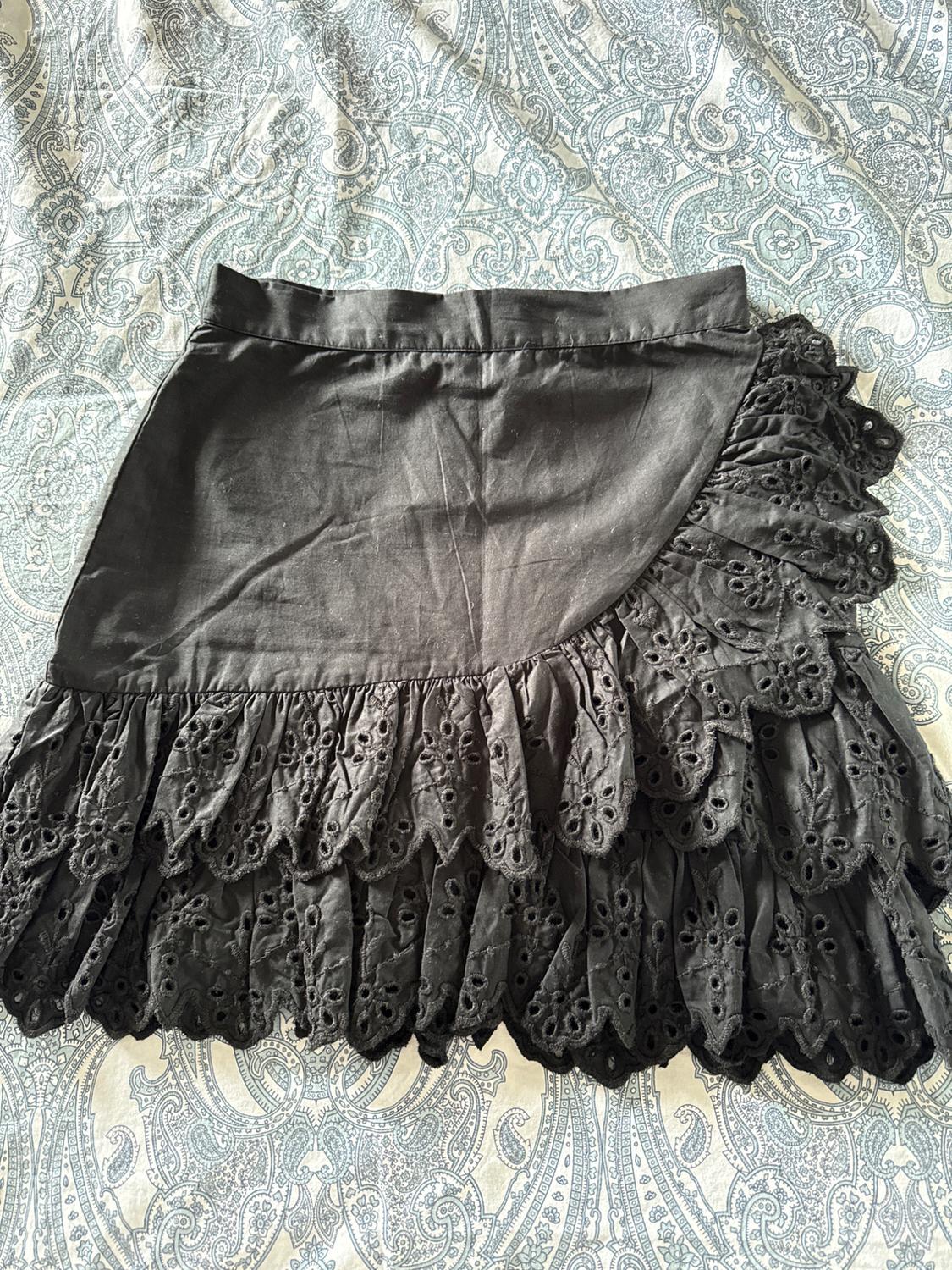 Black short skirt with asymmetrical ruffles and openwork embroidery, over a blue and white paisley print fabric. Relaxed style.