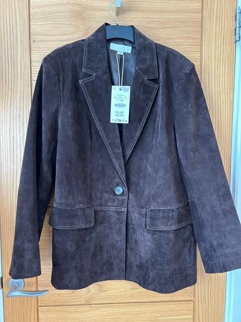 Brown suede jacket hanging on a wooden door, with a visible label in the centre.