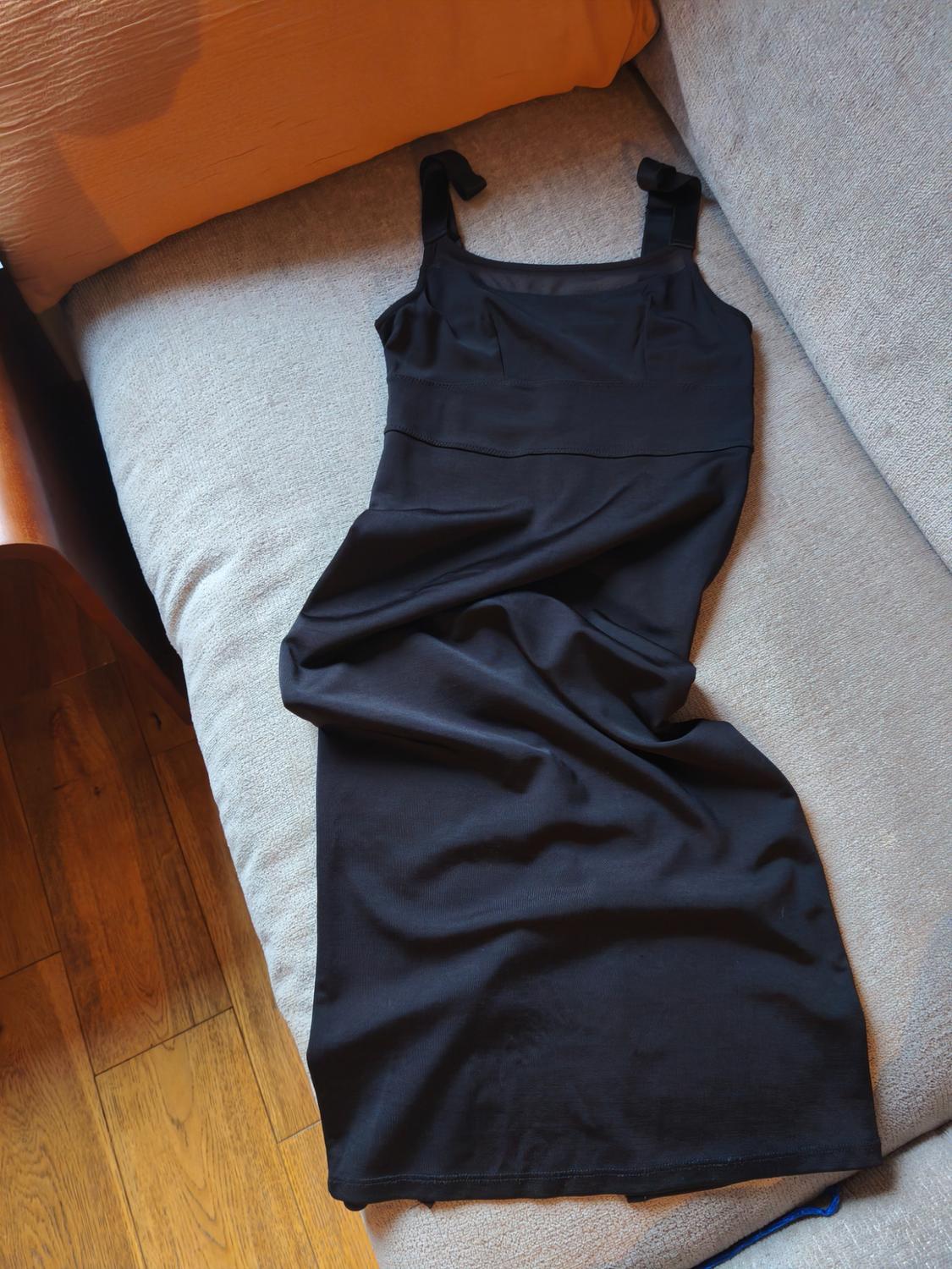 Black strappy dress on a grey sofa, with an orange cushion in the background and a wooden floor visible.