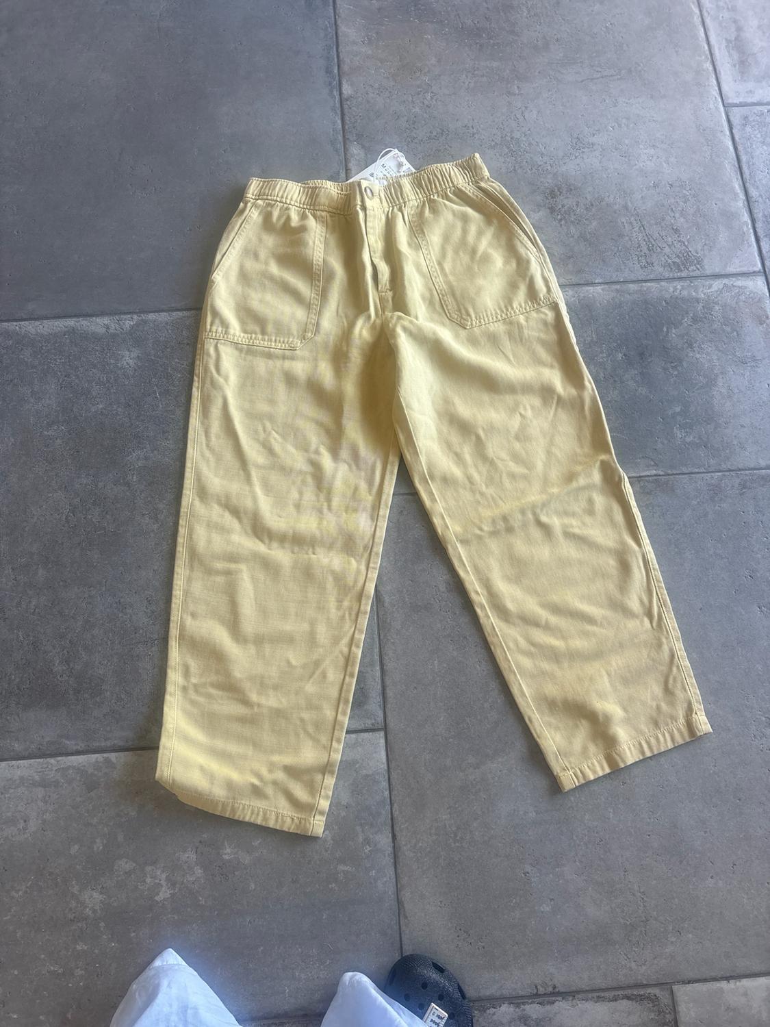 Pale yellow wide-leg trousers with an elasticated waist and front pockets, photographed from above on a grey tiled floor.