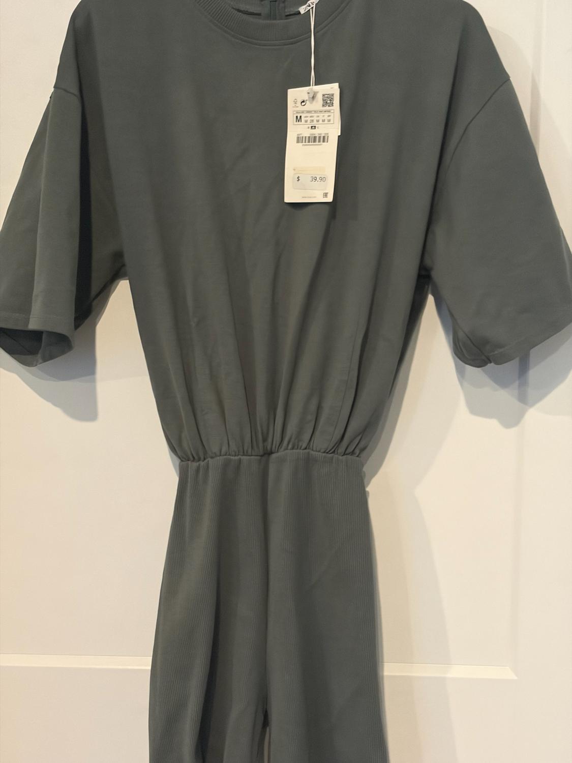 Grey short-sleeved garment with a gathered waist and ribbed texture, hanging on a white door. Label with the text: M $39.90.