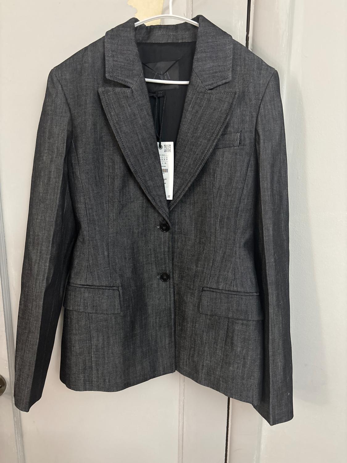 Dark grey blazer hanging on a hanger over a door. It features lapels, a two-button front fastening and flap pockets.