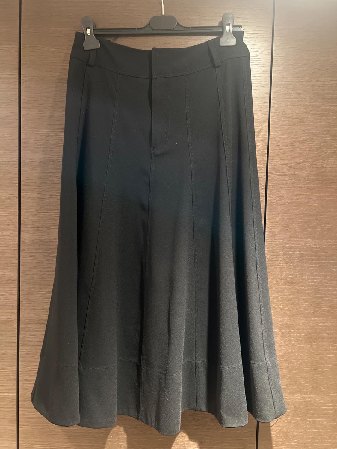 Plain black skirt hanging on a hanger against a brown wooden background. Classic design with subtle pleats.