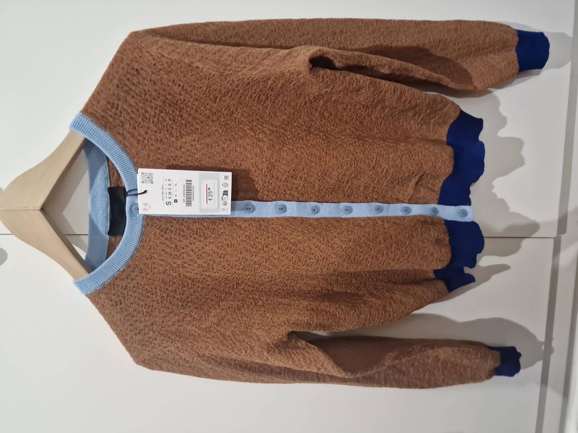 Textured brown cardigan on a hanger against a white background. Light blue collar and buttons, dark blue cuffs. Label with text: S, € 25.
