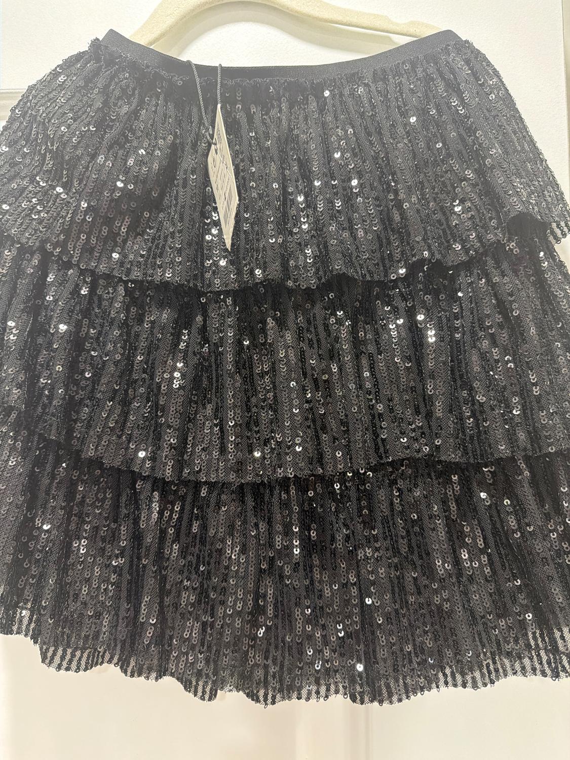 Black sequined skirt with layered ruffles, hanging on a beige hanger. Label visible at the top.