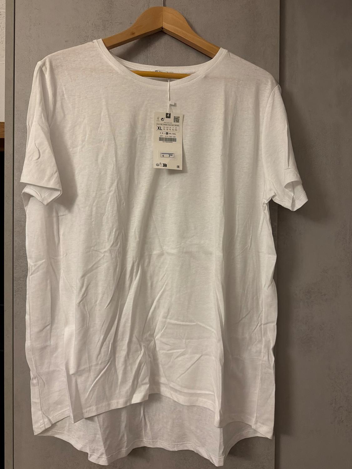 White short-sleeved T-shirt hanging on a wooden hanger, with a visible label indicating size XL. Grey background.