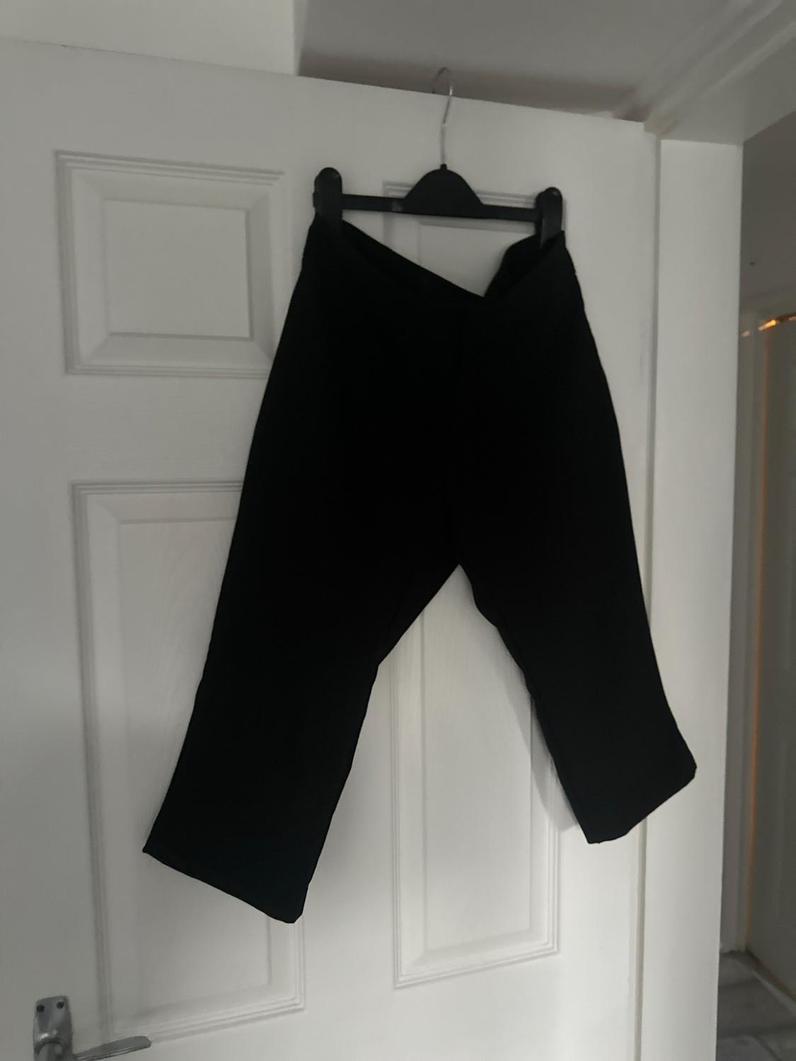 Black trousers hanging on a black hanger on a white internal door.