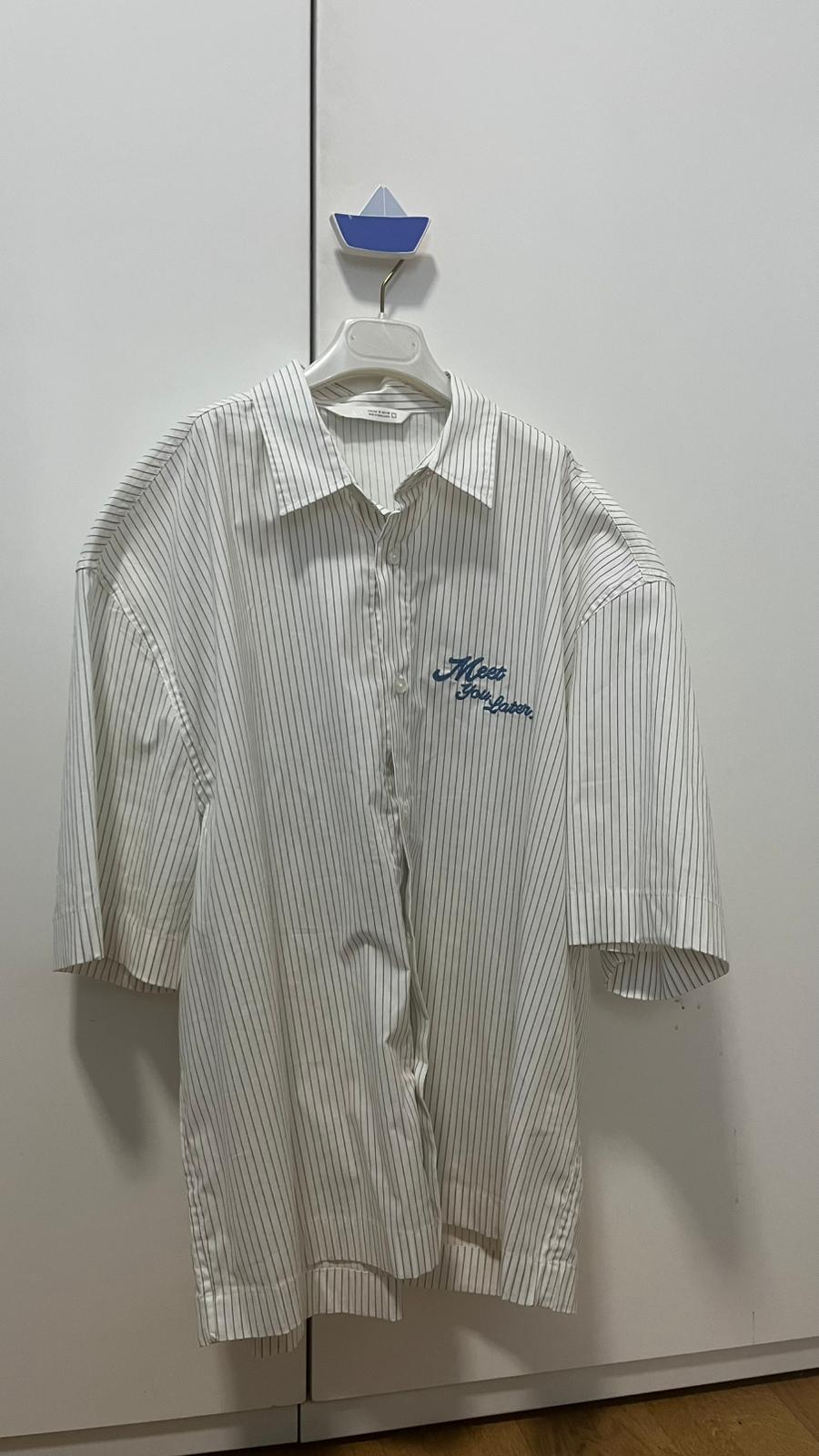 White shirt with fine stripes hanging on a blue boat-shaped hanger. Blue text on the chest: "Meet You Later".