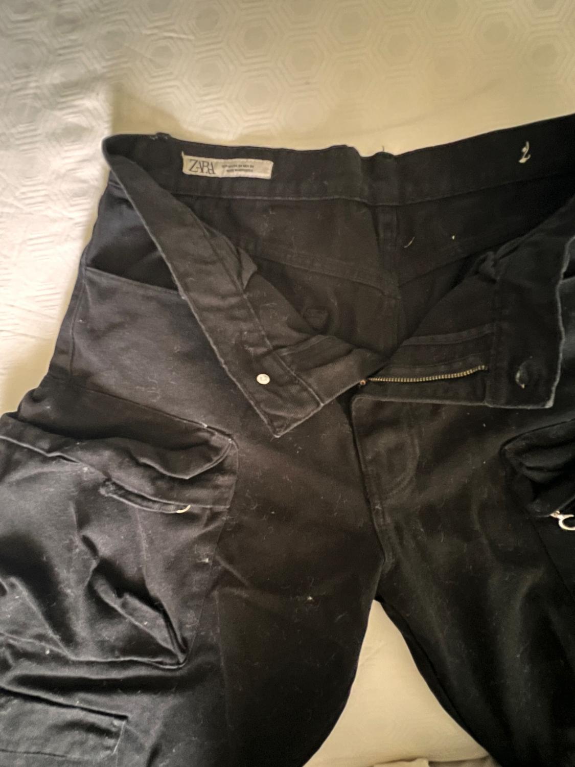 Unbuttoned black cargo pants with pockets on a white surface. Interior label reading ZARA.