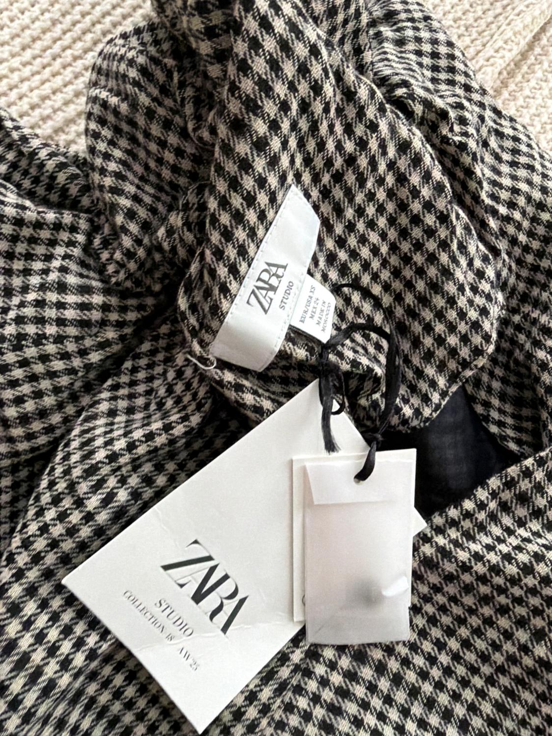 Zara Studio clothing label on black and white checkered fabric. Visible text: "ZARA STUDIO COLLECTION AW23".